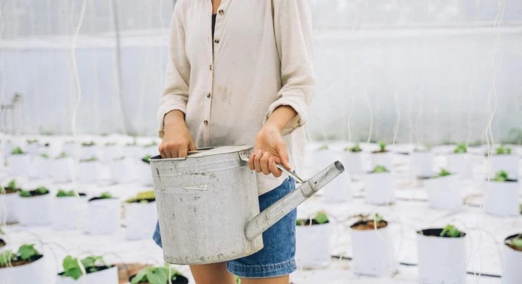 A woman waters plants in a lush home garden with a metal watering can.
