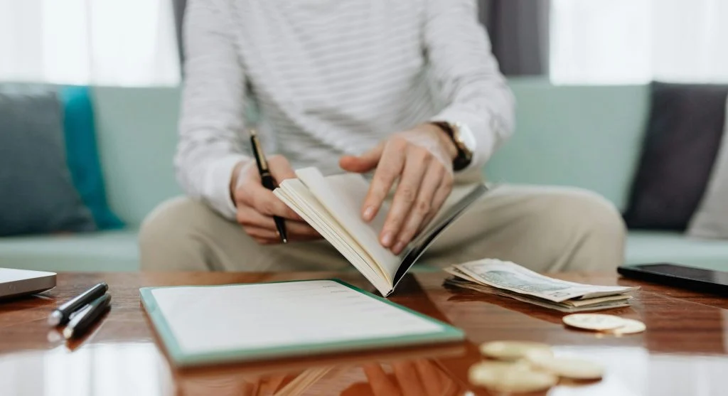 Person reviewing a garden journal or seed catalog indoors near a rainy window 