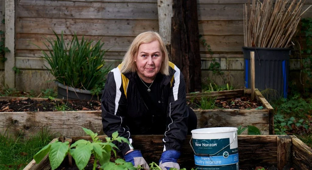 Gardener adding fresh compost to the top of a raised bed to replenish soil level